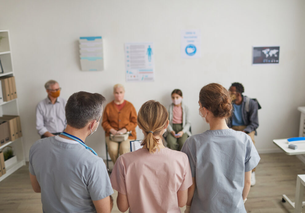 Back view portrait of group of doctors looking at patients waiting in line in vaccination center or clinic, copy space